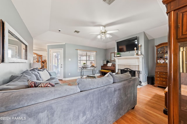 living room featuring a tiled fireplace, a raised ceiling, ceiling fan, and light hardwood / wood-style flooring