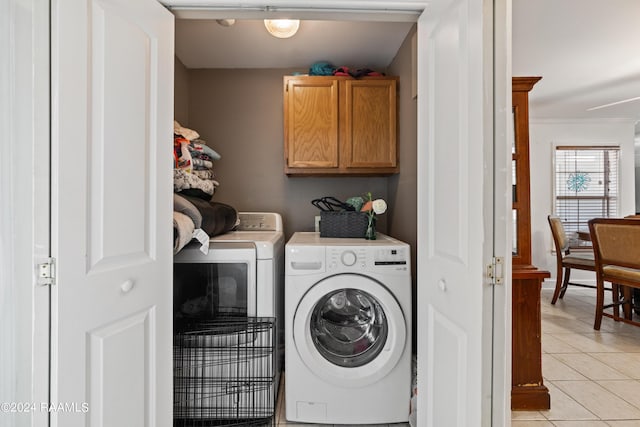 laundry room featuring crown molding, cabinets, washer and dryer, and light tile patterned floors