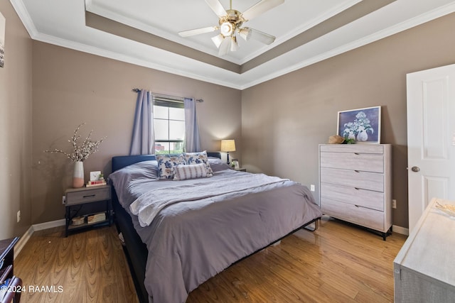 bedroom featuring crown molding, ceiling fan, a tray ceiling, and light hardwood / wood-style flooring