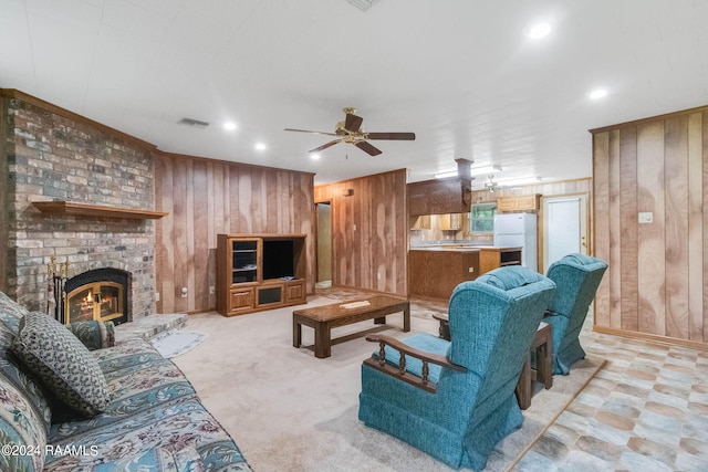 carpeted living room with wooden walls, a brick fireplace, and ceiling fan