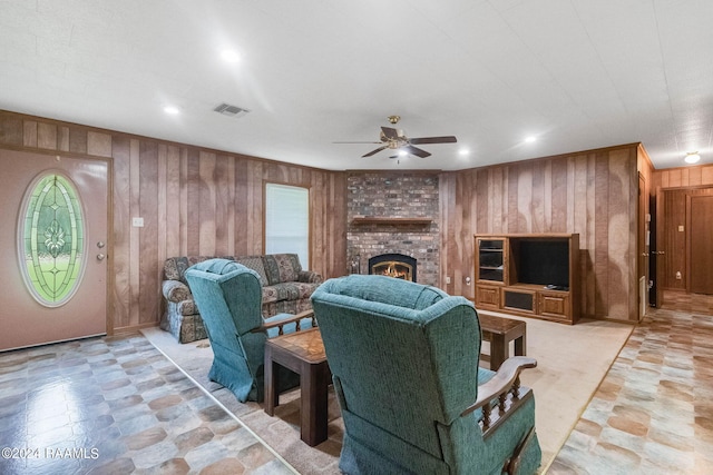 living room featuring a fireplace, ceiling fan, and wooden walls