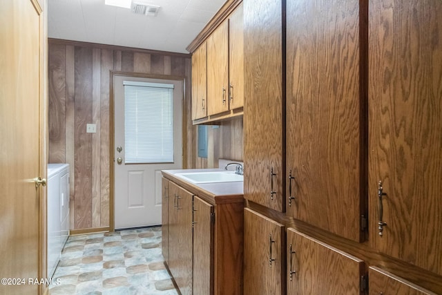 clothes washing area with sink, cabinets, wooden walls, and washer and clothes dryer