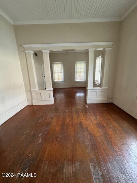 empty room featuring decorative columns, crown molding, and dark wood-type flooring