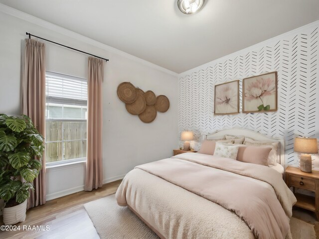 bedroom with baseboards, wallpapered walls, ornamental molding, light wood-style floors, and an accent wall