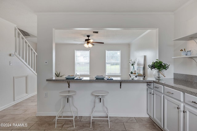 kitchen with open shelves, a breakfast bar area, a ceiling fan, and ornamental molding