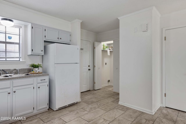 kitchen with ornamental molding, a sink, white cabinetry, freestanding refrigerator, and baseboards