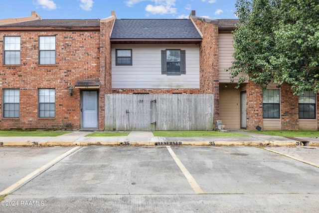 view of front facade featuring fence, uncovered parking, brick siding, and roof with shingles