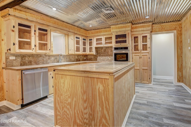 kitchen with sink, wooden walls, light brown cabinetry, a kitchen island, and appliances with stainless steel finishes