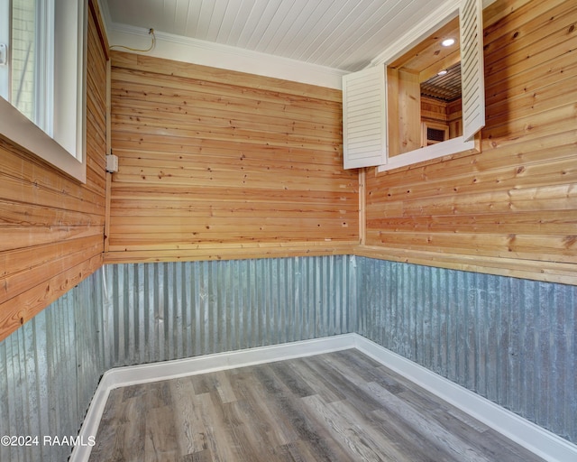 empty room with wooden walls, crown molding, and wood-type flooring