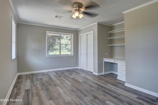 unfurnished bedroom featuring built in desk, wooden walls, ceiling fan, light wood-type flooring, and ornamental molding