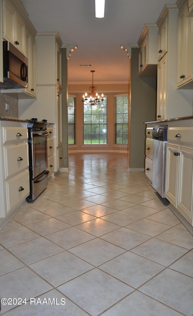 kitchen featuring light tile patterned floors, an inviting chandelier, appliances with stainless steel finishes, cream cabinetry, and ornamental molding