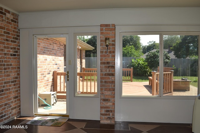 doorway to outside featuring a wealth of natural light, ornamental molding, and brick wall