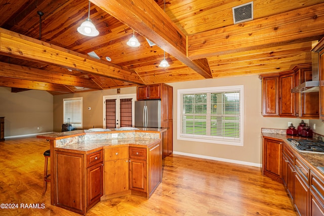 kitchen featuring a center island, light wood-type flooring, stainless steel appliances, beam ceiling, and a breakfast bar