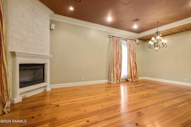 unfurnished living room featuring light wood-type flooring, a large fireplace, ornamental molding, and an inviting chandelier