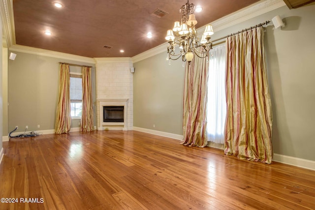 unfurnished living room featuring light hardwood / wood-style flooring, brick wall, a fireplace, a notable chandelier, and ornamental molding