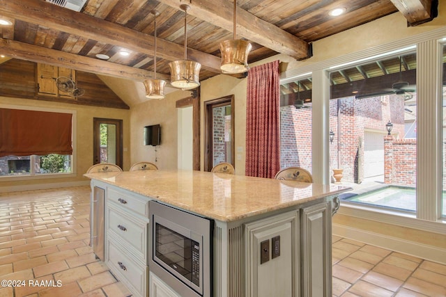 kitchen with stainless steel microwave, white cabinets, beamed ceiling, and pendant lighting