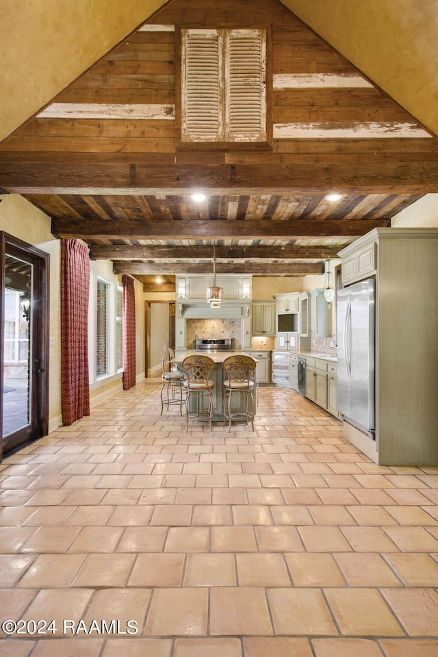 kitchen featuring light tile patterned flooring, beam ceiling, a center island, stainless steel fridge, and a kitchen bar