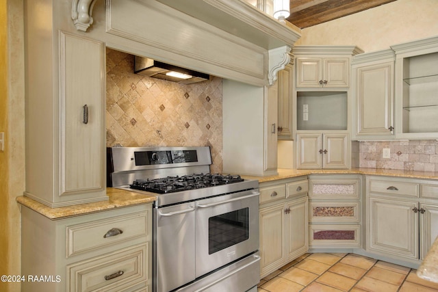 kitchen with double oven range, light stone countertops, beam ceiling, light tile patterned floors, and decorative backsplash