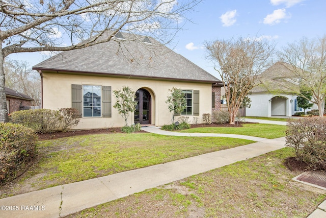 view of front of home with a front yard, roof with shingles, and stucco siding