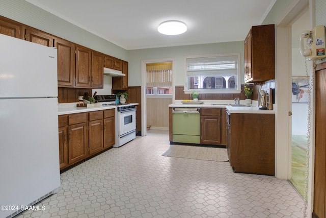 kitchen with sink, white appliances, ornamental molding, and wooden walls