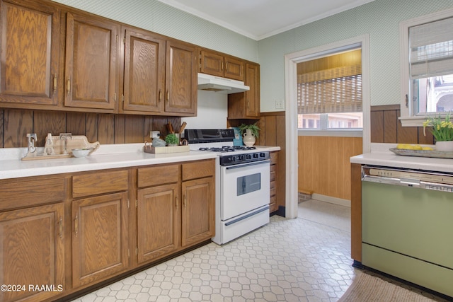 kitchen with ornamental molding, white appliances, wooden walls, and plenty of natural light