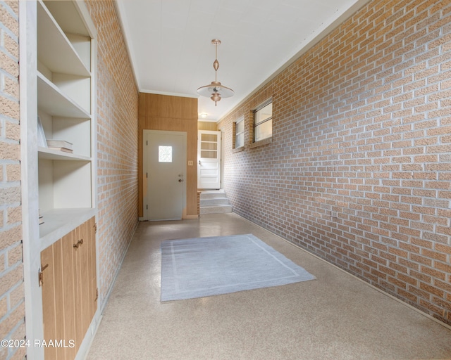 doorway to outside featuring wood walls, plenty of natural light, brick wall, and crown molding