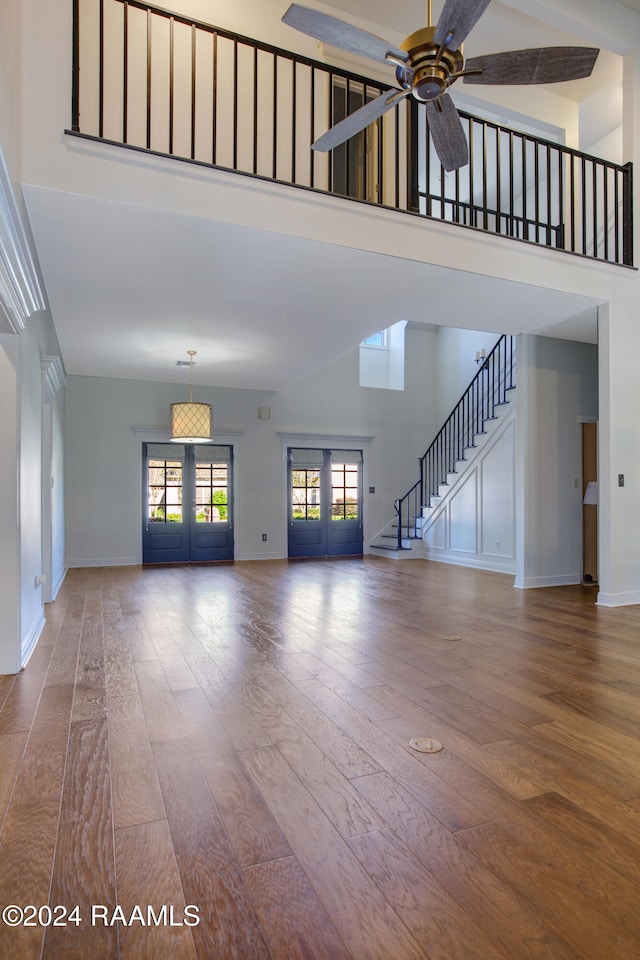 unfurnished living room featuring hardwood / wood-style floors, french doors, ceiling fan, and a high ceiling