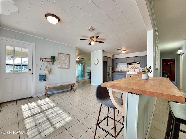 kitchen with a kitchen bar, tasteful backsplash, gray cabinetry, black fridge, and light tile patterned flooring