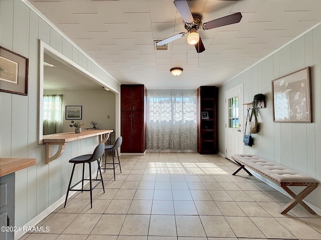 interior space with ceiling fan, crown molding, and wooden walls