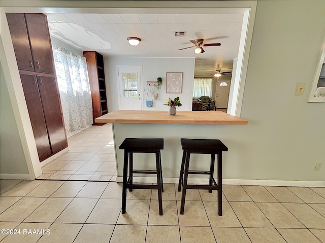 kitchen featuring kitchen peninsula, a kitchen bar, butcher block countertops, and light tile patterned flooring