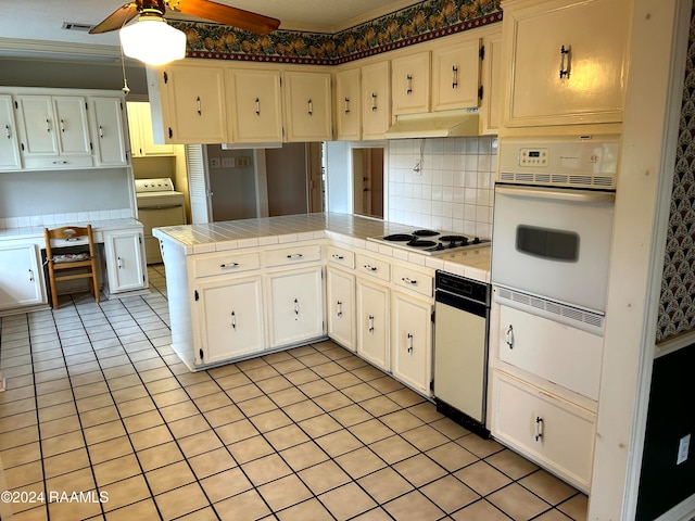 kitchen featuring tile counters, kitchen peninsula, white cabinetry, white appliances, and washer / dryer