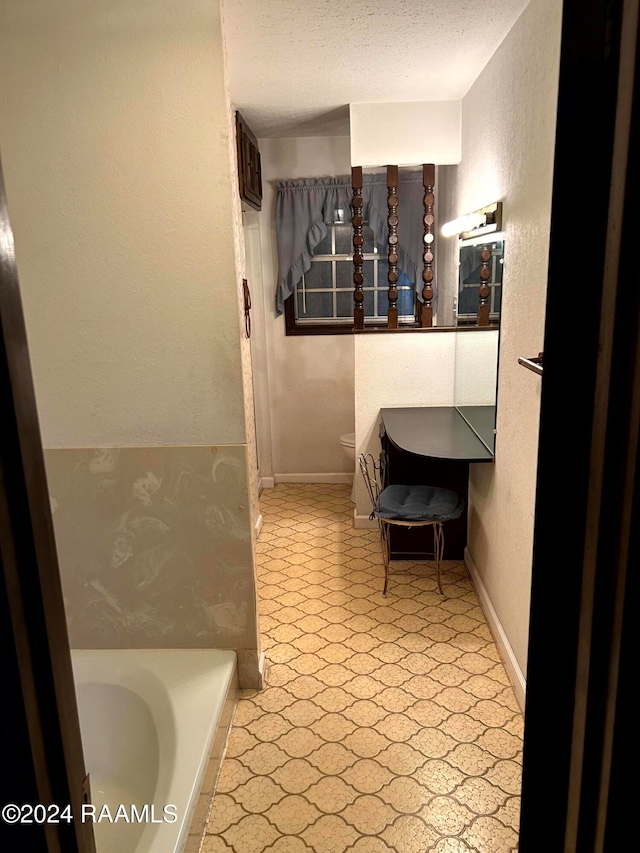 bathroom with toilet, a textured ceiling, and a tub