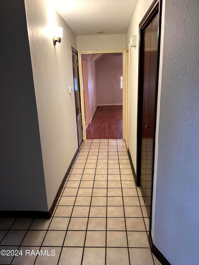 corridor with a textured ceiling and light tile patterned flooring