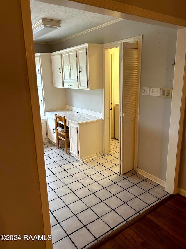 kitchen featuring tile countertops, a textured ceiling, crown molding, white cabinetry, and light wood-type flooring