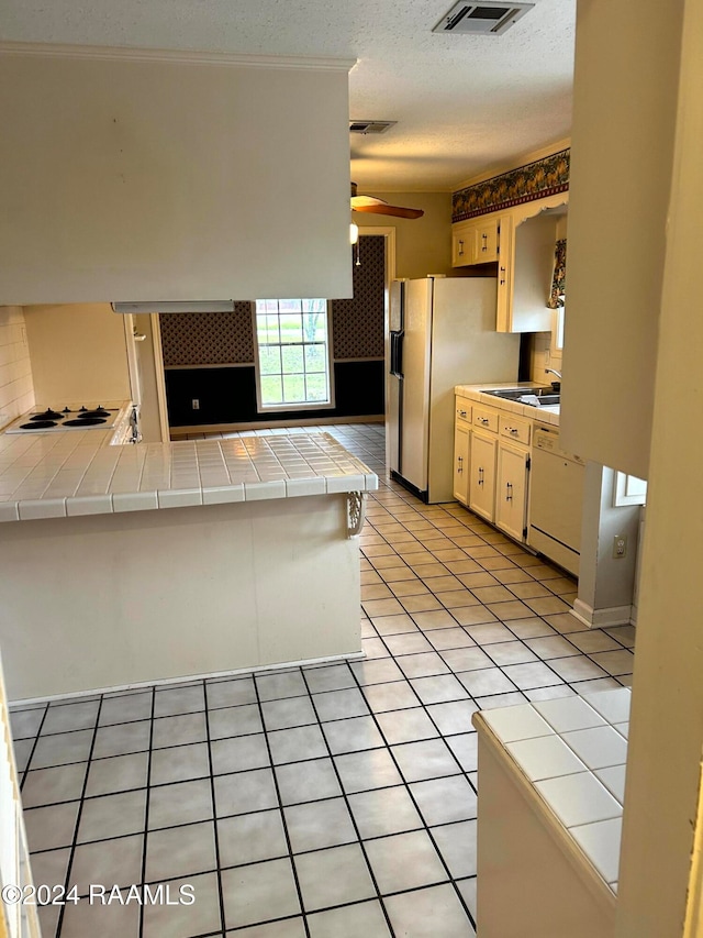 kitchen with tile countertops, kitchen peninsula, sink, light tile patterned floors, and ceiling fan