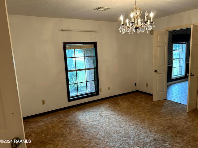 carpeted empty room with a textured ceiling and a notable chandelier