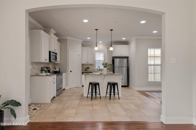 kitchen with hanging light fixtures, appliances with stainless steel finishes, a kitchen island, light stone countertops, and white cabinets