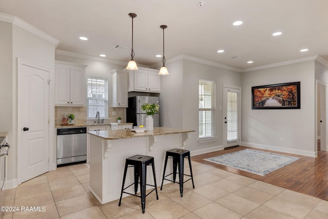 kitchen featuring a kitchen island, appliances with stainless steel finishes, white cabinetry, sink, and light stone counters