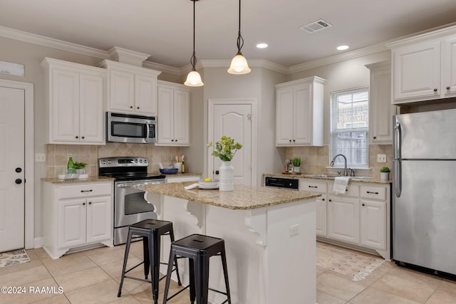 kitchen featuring white cabinets, hanging light fixtures, a center island, stainless steel appliances, and light stone countertops