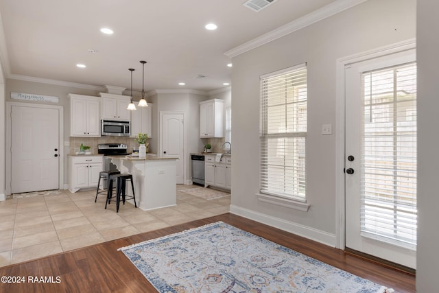 kitchen with a kitchen island, a breakfast bar, pendant lighting, white cabinetry, and stainless steel appliances