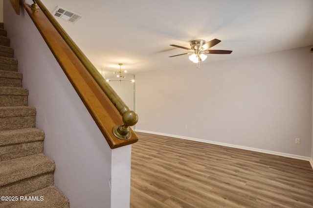 staircase with wood-type flooring and ceiling fan with notable chandelier