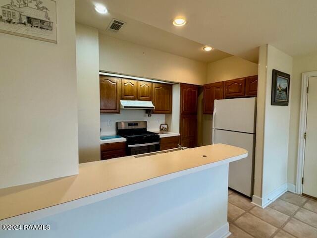 kitchen with white refrigerator, stainless steel range oven, light tile patterned floors, and kitchen peninsula