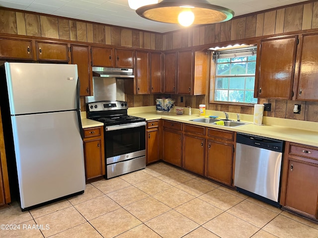 kitchen featuring wooden walls, light tile patterned flooring, appliances with stainless steel finishes, and sink