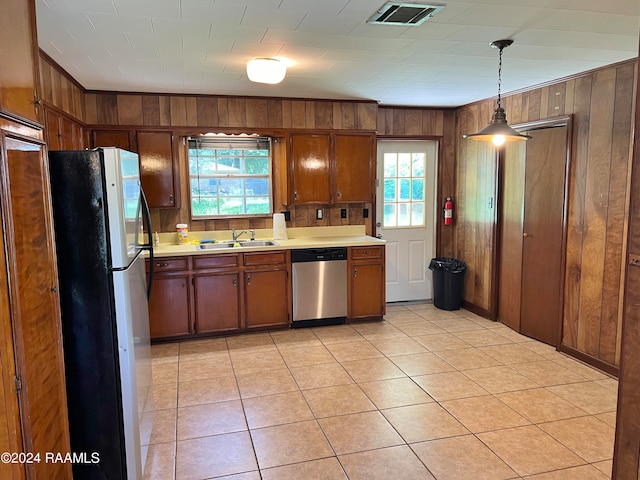 kitchen featuring a healthy amount of sunlight, fridge, wooden walls, and stainless steel dishwasher