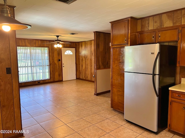 kitchen with light tile patterned flooring, wood walls, stainless steel refrigerator, and ceiling fan