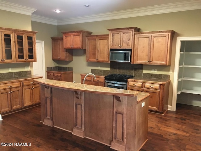 kitchen with dark hardwood / wood-style floors, a kitchen breakfast bar, a kitchen island with sink, stainless steel appliances, and crown molding