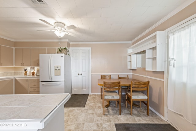 kitchen with light tile patterned flooring, ceiling fan, white fridge with ice dispenser, crown molding, and tile countertops