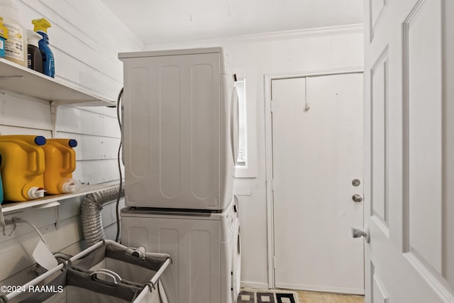 laundry area featuring stacked washer and clothes dryer, ornamental molding, and light tile patterned floors