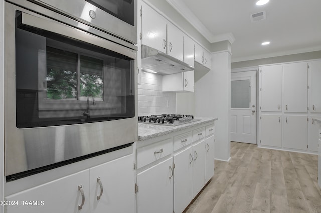 kitchen with appliances with stainless steel finishes, tasteful backsplash, light hardwood / wood-style floors, white cabinetry, and ornamental molding