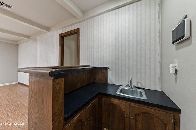 bar with dark brown cabinetry, sink, beam ceiling, and light hardwood / wood-style flooring